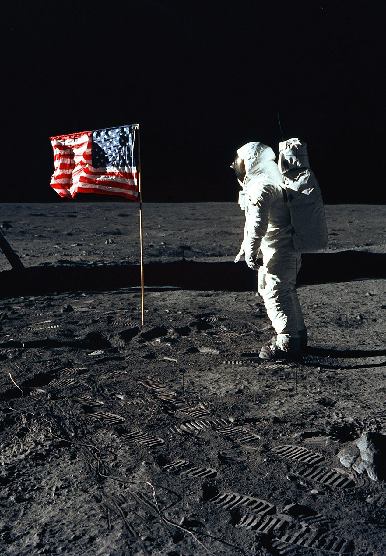 Astronaut Buzz Aldrin stands next to the US flag on the moon during the Apollo 11 mission. The lunar module is to the left, with distinct astronaut footprints in the moon's soil. Photo taken by mission commander, Neil A. Armstrong, using a 70mm Hasselblad camera.