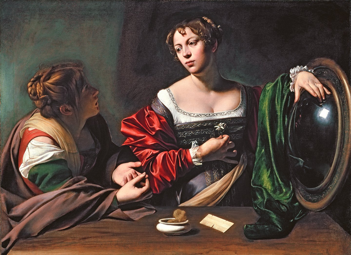 The painting depicts two women sitting at a table with a mirror in front of them. One woman is holding a small flower in her hand and the other is looking into the mirror. Both women are wearing elaborate clothing, with one wearing a red dress and the other wearing a green dress. The background is a dimly lit room with a window in the background.