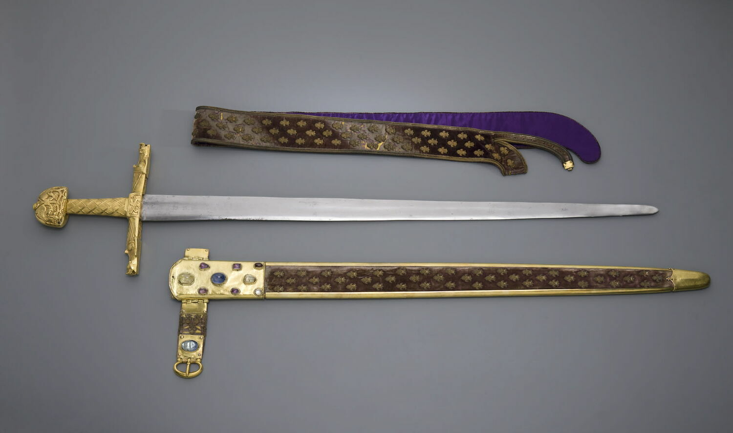 A photo of sword with a golden hilt, a golden scabbard, and a sword sling covered Fleur-de-lis symbols.