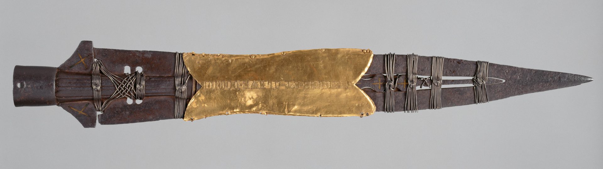 A photograph of an ancient lance head partially covered in gold.