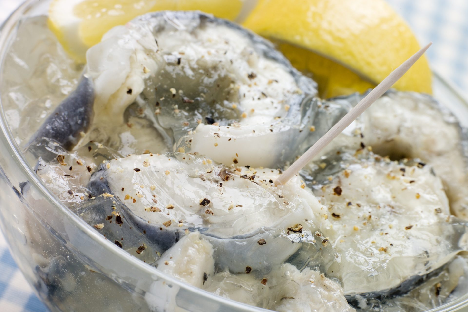 A photograph depicting chunks of gelatinized eels in a transparent bowl. A toothpick is sticking out from one of the chunks. There is a lemon slice in the bowl.