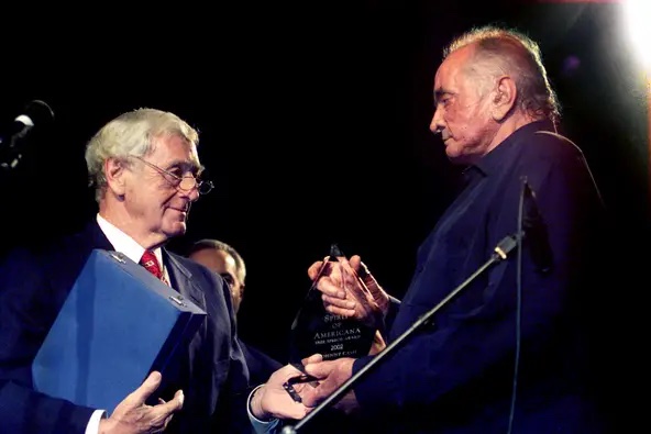A photograph of two men on stage holding an award.