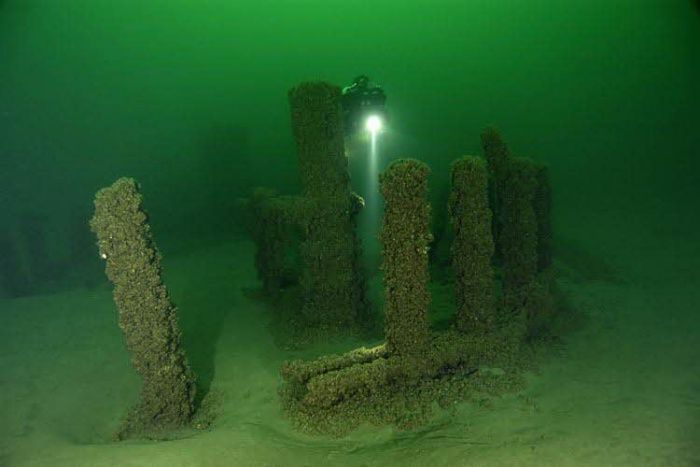 The image shows a group of stone monoliths that are submerged in water. They appear to be old and weathered, with some of the posts leaning to one side.