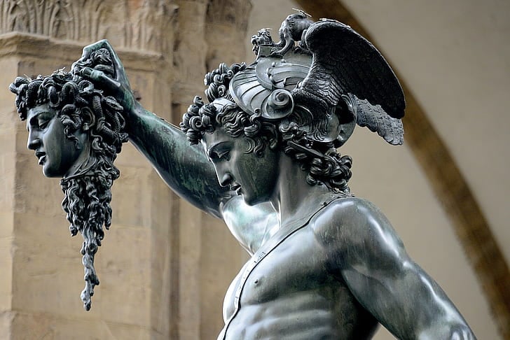 A bronze statue of a muscular man holding a severed head in his right hand. The man is Perseus, a hero from Greek mythology who killed Medusa, a monster with snakes for hair. The head he holds is Medusa’s. The statue is located in the Loggia dei Lanzi, a public square in Florence, Italy.