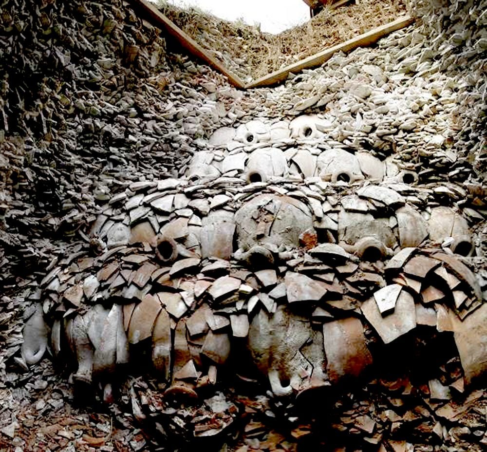 The image is of a large pile of ceramic shards stacked on top of each other in the shape of a pyramid. The shards appear to be very old and weathered. There is a wooden beam running through the middle of the pile of ceramic shards.