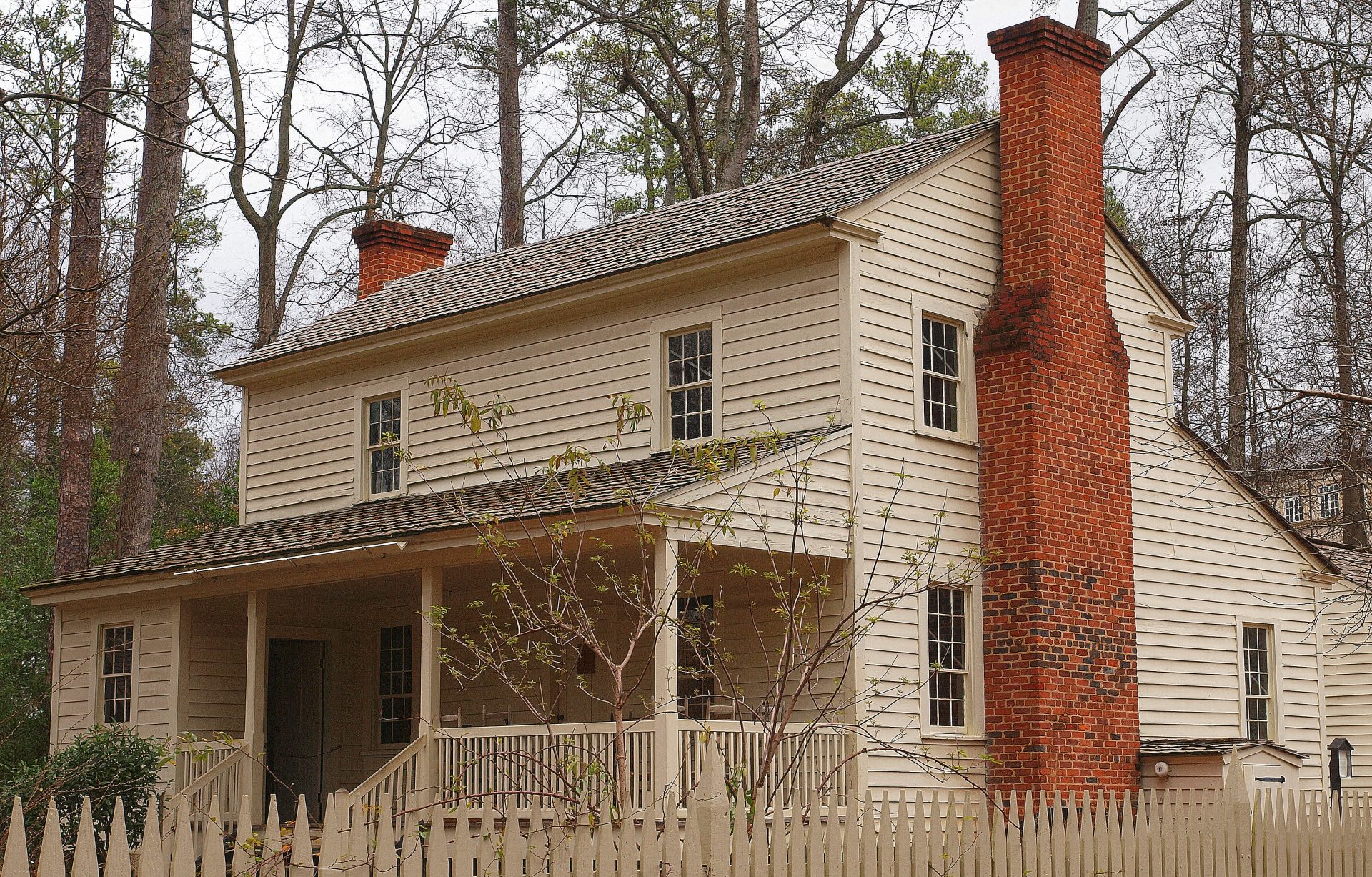 A photo of the Tullie Smith House in the Atlanta History Center, a wood plank sided two story house with a brick chimney.