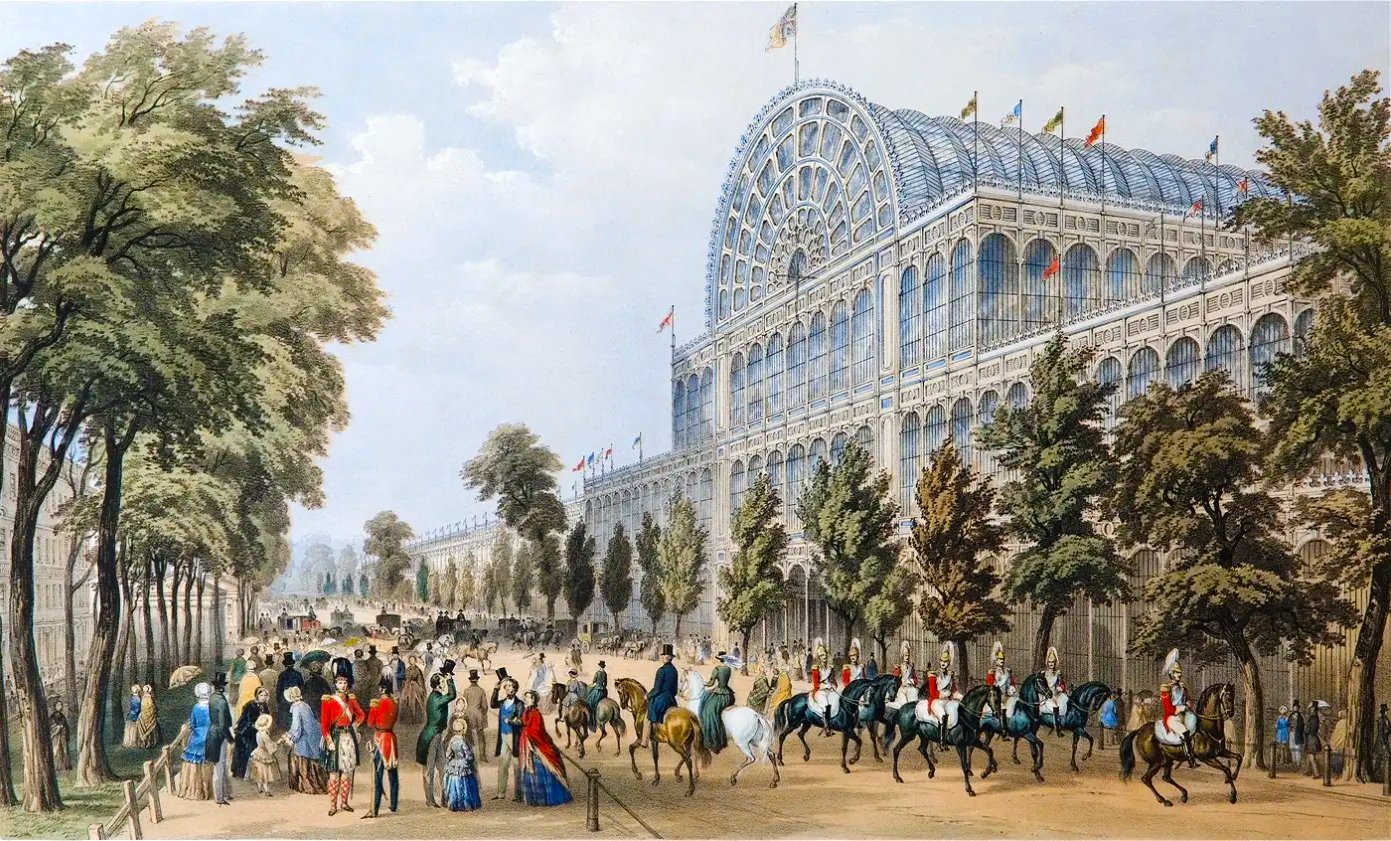 This is an illustration of the Crystal Palace in Hyde Park, London, which hosted the Great Exhibition in 1851. The illustration shows the palace made out of glass and iron. It depicts a crowd of people in front of the palace, some on horseback and some on foot. The palace is surrounded by trees and there is a blue sky in the background.
