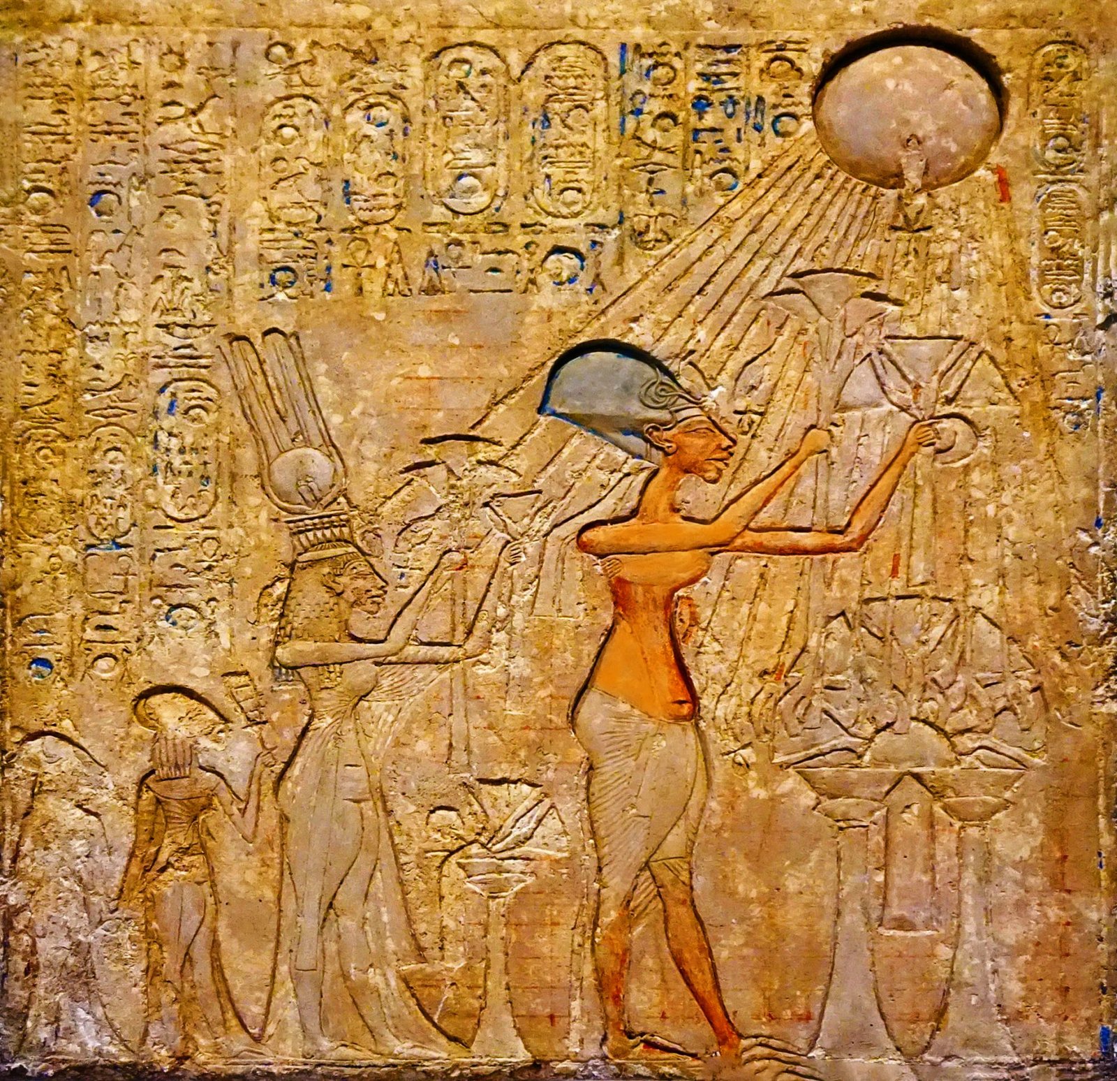 Relief depicting Akhenaten and Nefertiti, alongside their two daughters, in a reverent posture worshiping the sun disk, Aten. The royal family is intricately detailed, showcasing their unique Amarna-style features and traditional ceremonial attire as they offer their devotion to the central deity of their reign.