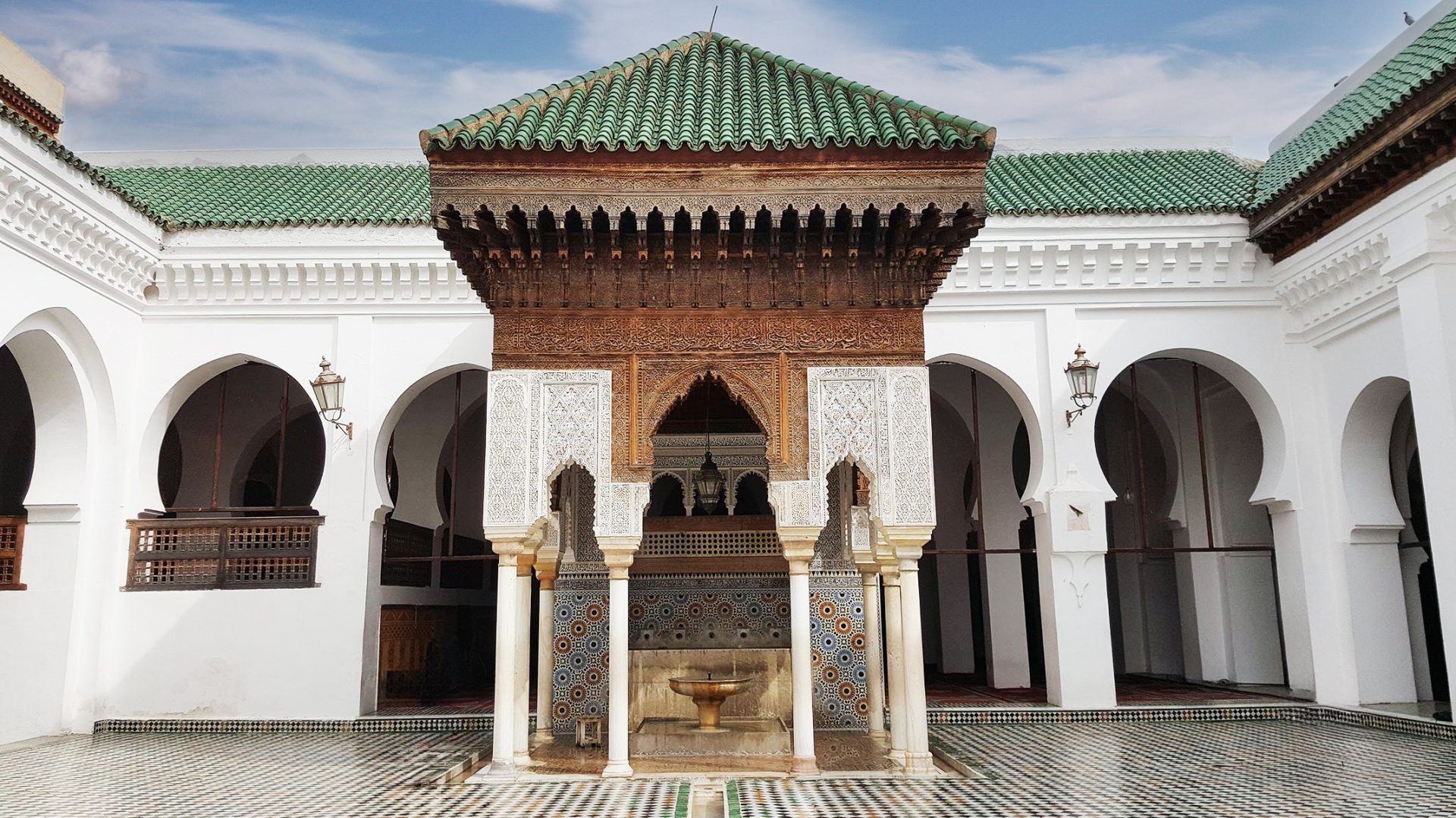 A courtyard in a Moroccan Al-Qarawiyyin University with a fountain, arches, columns, and colorful tiles.