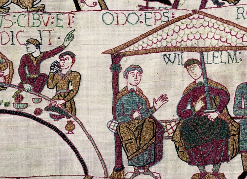 A tapestry depicting two men sitting on a bench under a roof. in the background two men are having a meal.