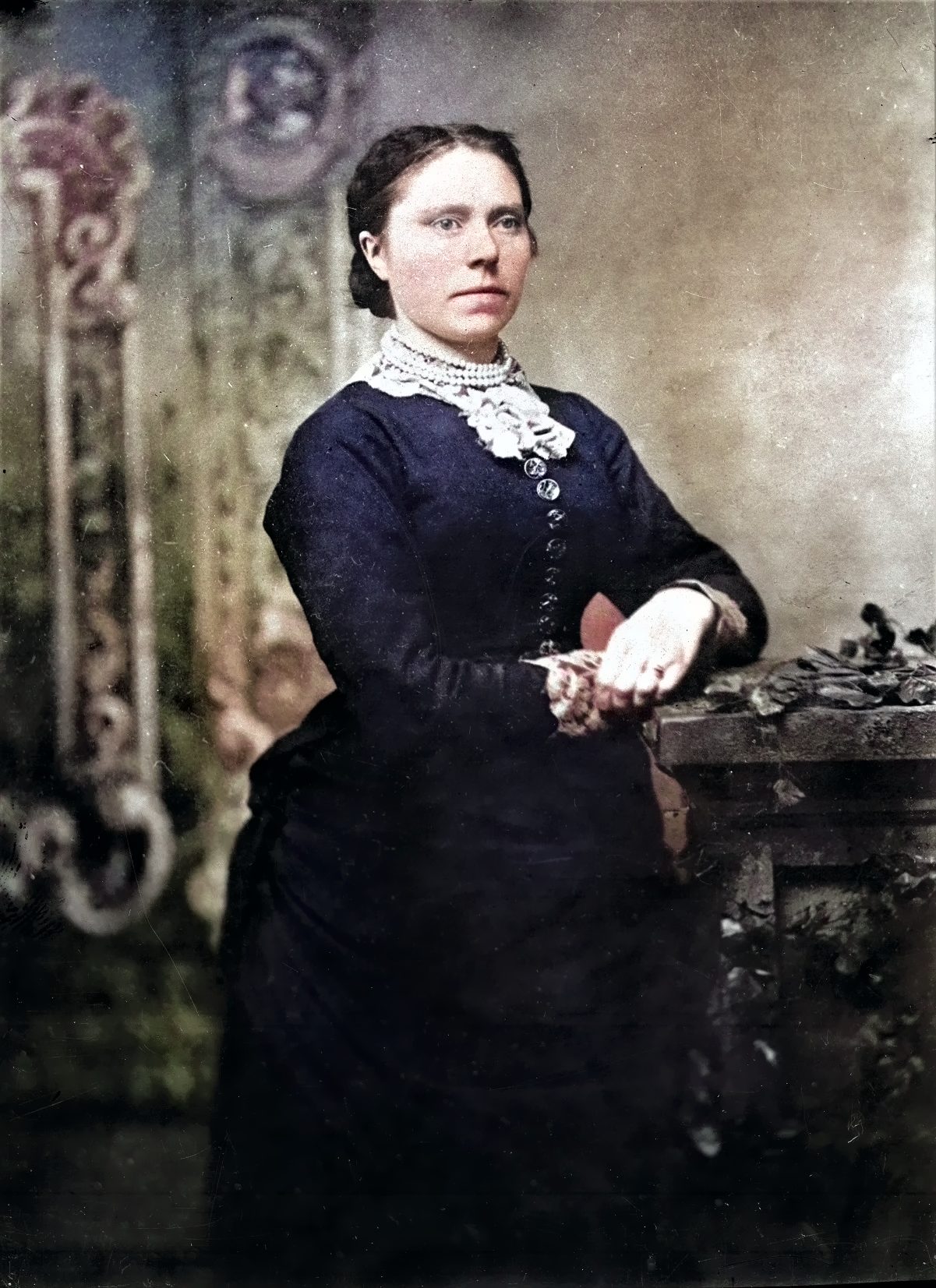 This is an image of a woman in an old-fashioned dress standing in front of a large wooden table. She is wearing a blue dress with a lace collar.