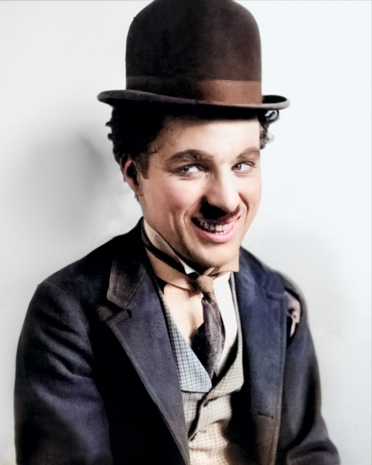 This image features Charlie Chaplin, a man wearing a black fedora hat, with a white background. He is smiling and has an air of confidence about him. His face is framed by the brim of his hat, which casts shadows on his cheeks and forehead. The man's clothing consists of a dark suit jacket over a light-colored shirt and tie, completing the look with classic style. This portrait captures Charlie Chaplin in all his iconic glory - from the signature bowler hat to the mischievous smile that made him famous around the world.