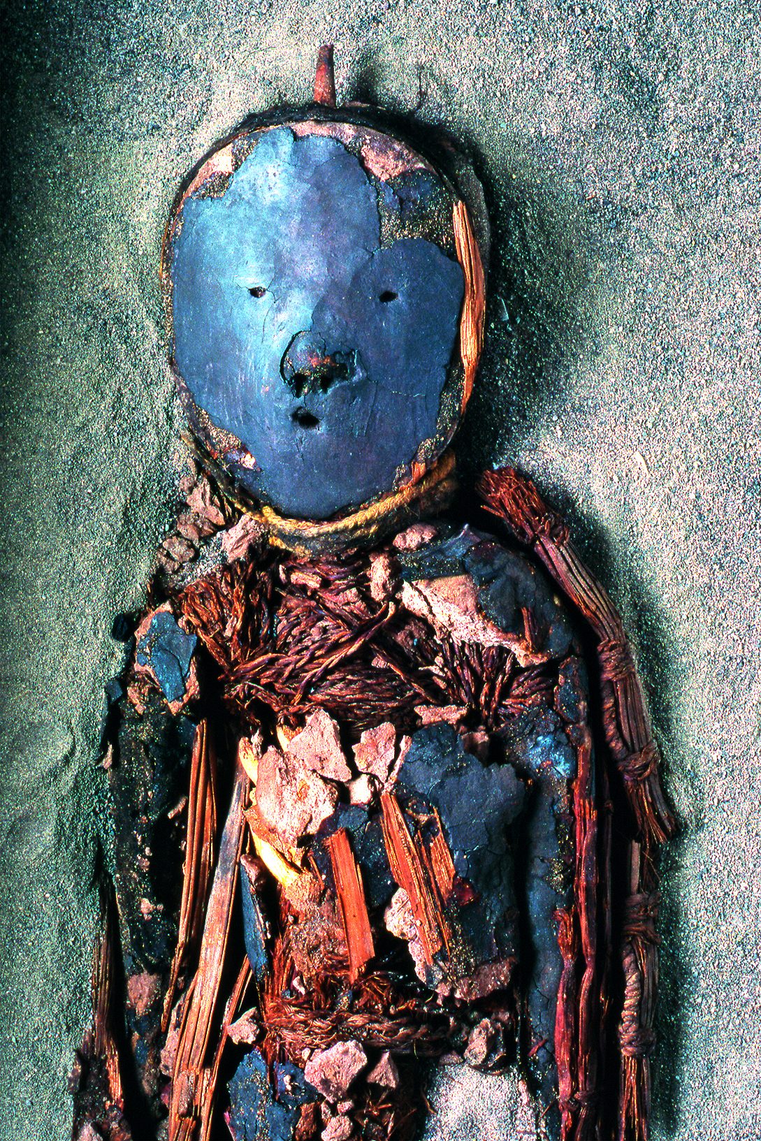 An image of a mummy with a bright blue mask covering the face. The internal organs are exposed.