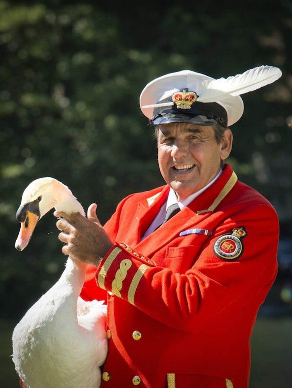 A photograph featuring a smiling man in a red coat and a hat holding a swan.