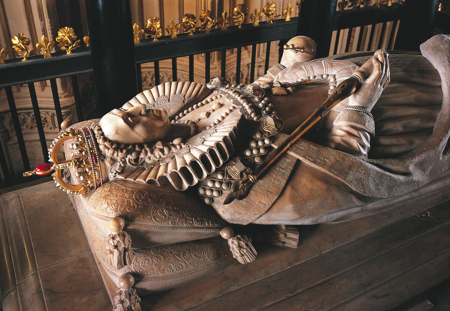 A photograph of the tomb of Elizabeth I at Westminster Abbey. The lid is a an elaborate stone sculpture of the queen in full royal garb lying on top of pillows.