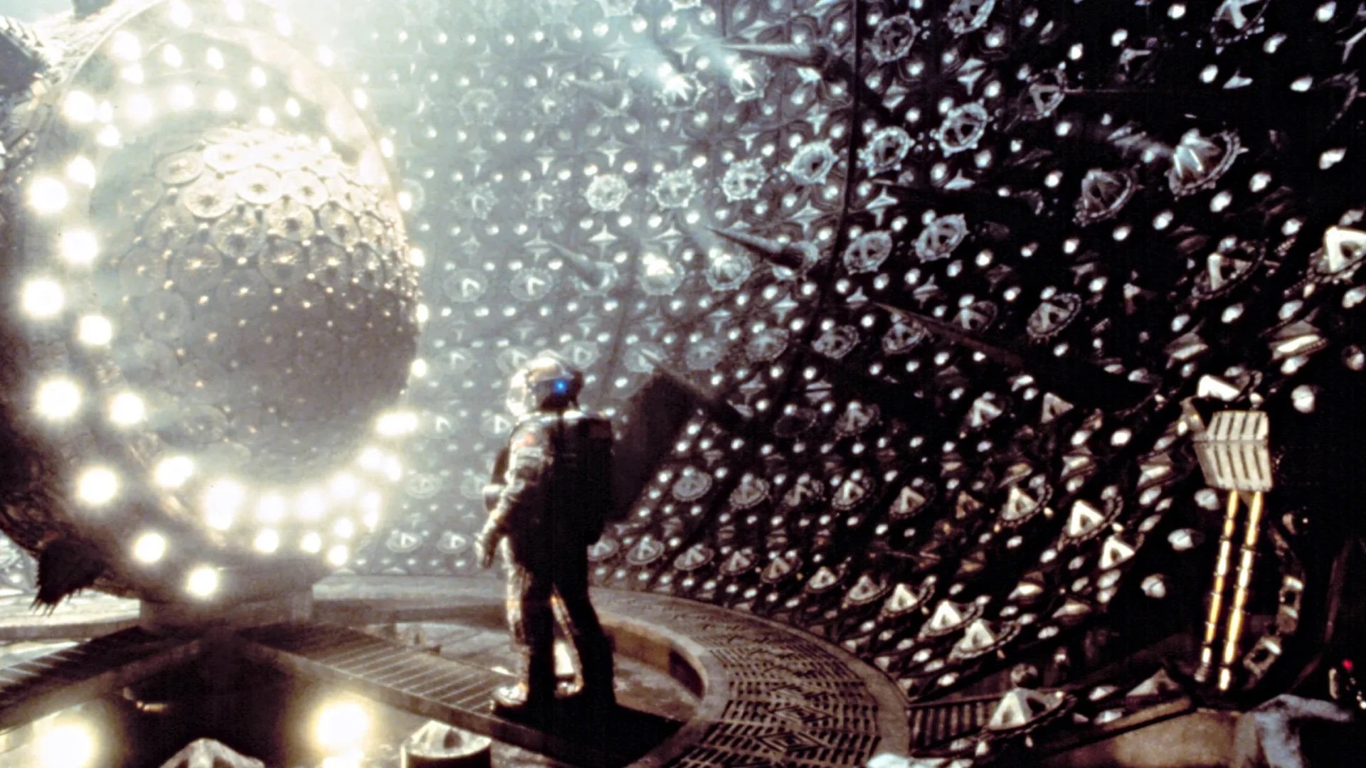 A man in a space suit looking at a futuristic looking reactor.