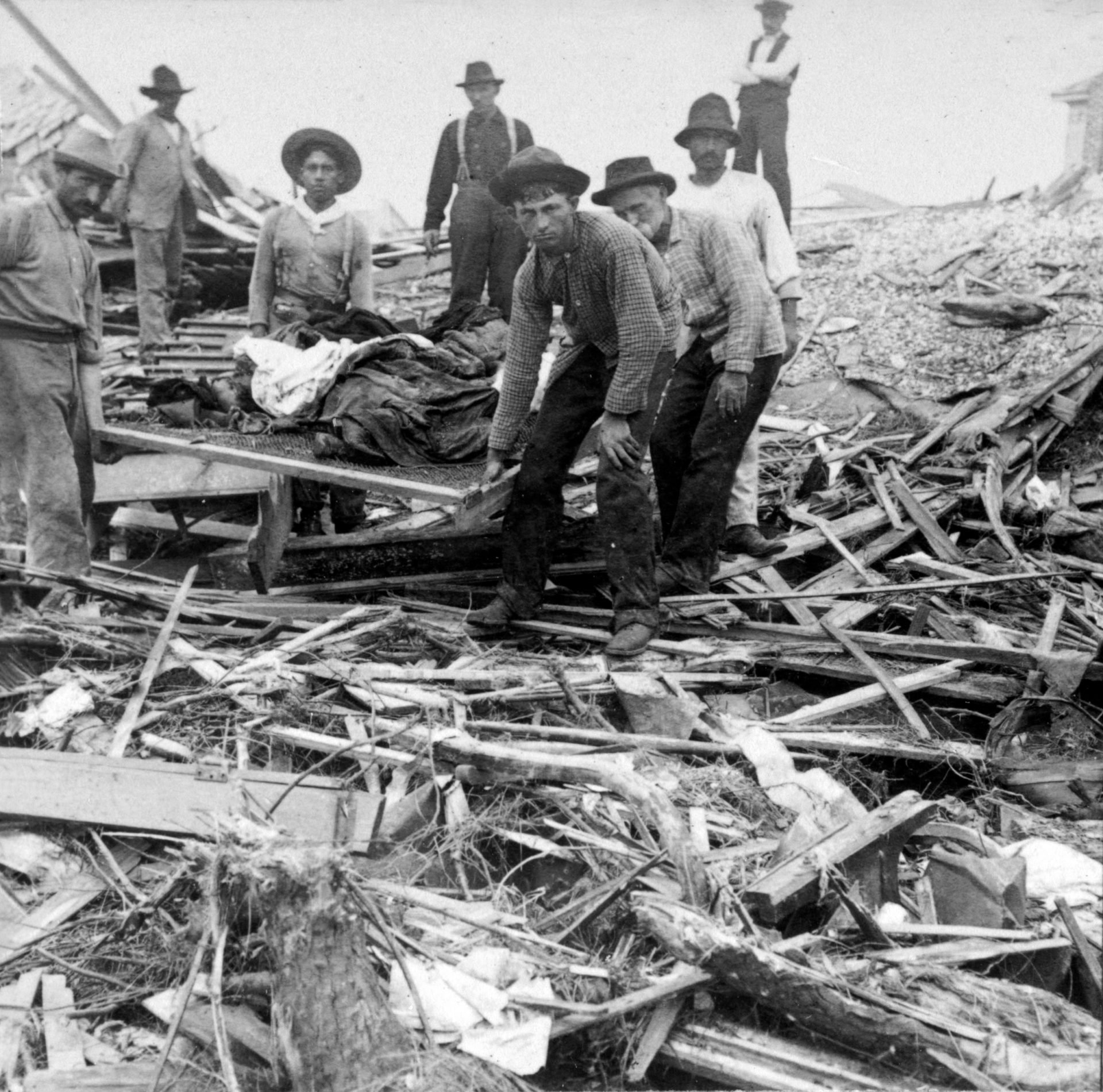 Men carrying bodies on a stretcher, surrounded by wreckage of the hurricane and flood, Galveston, Texas.