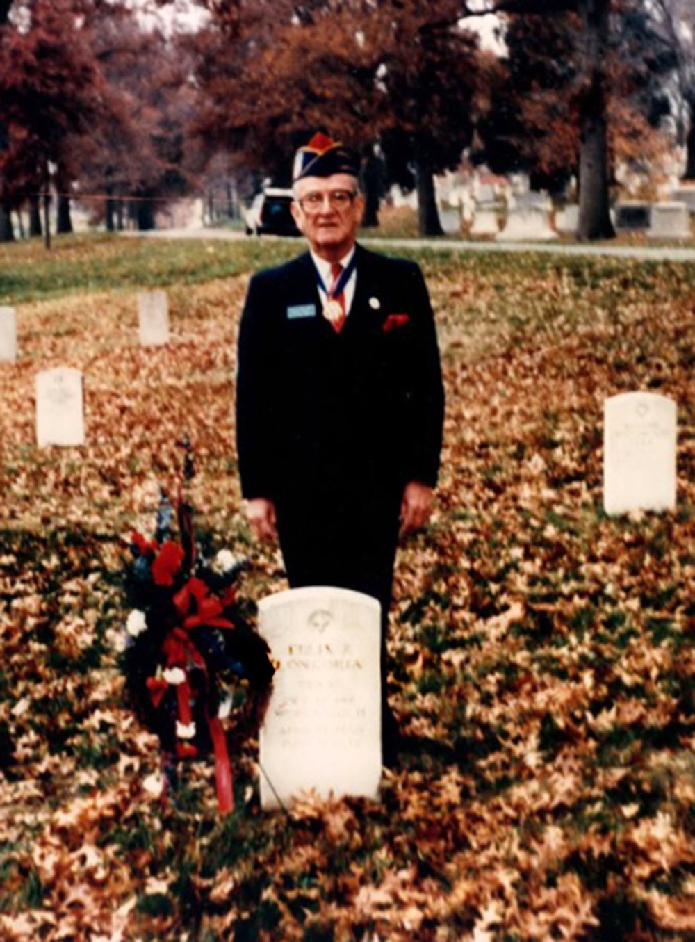 Dr. Hector P. Garcia standing next to Felix Longoria Gravestone. The ground is covered by fall leaves. Dr. Hector P. Garcia is wearing medals.
