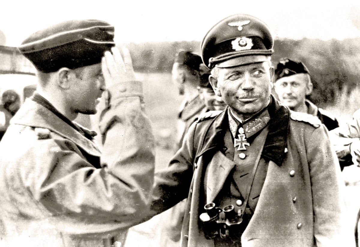 A black and white photo of General Heinz Guderian in military uniform with medals and cap being saluted by a soldier.