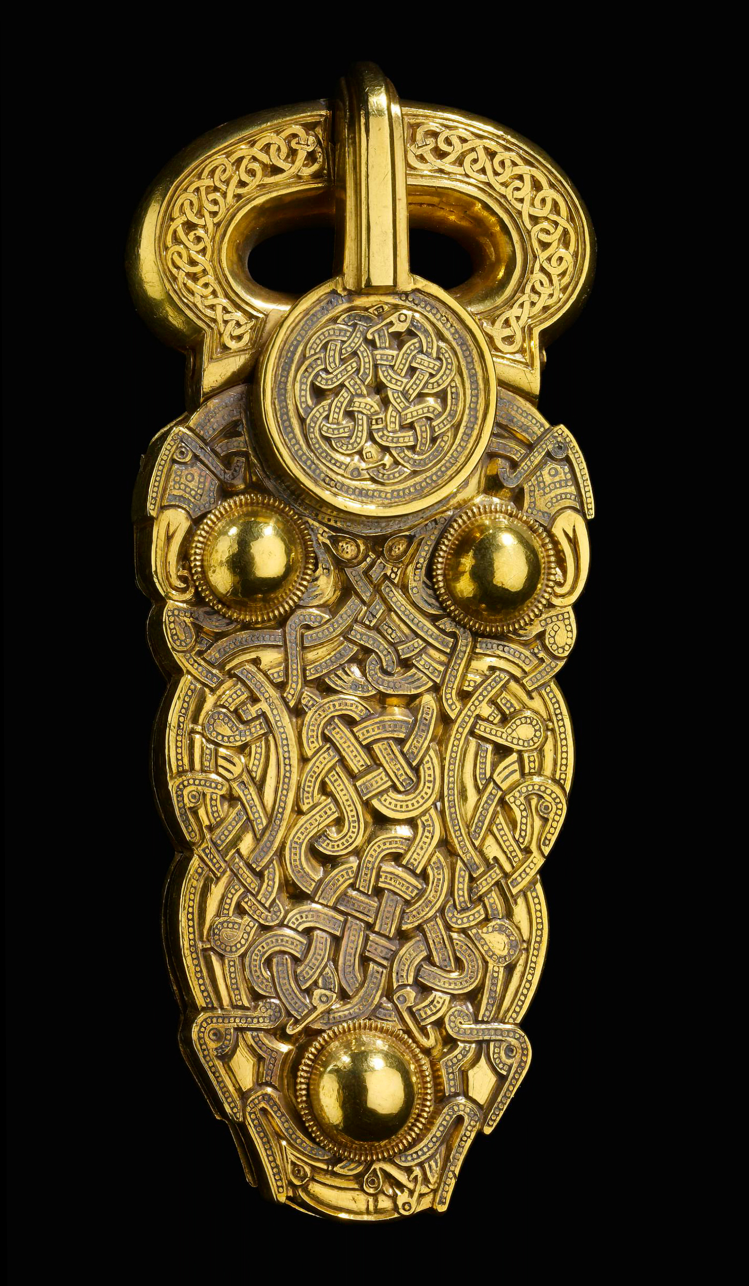 Gold belt-buckle, hollow with cast ornament. The upper surface is covered entirely with zoomorphic interlace, the design picked out in tiny punched circles and inlaid (except on the loop) in niello. Three large plain hemispherical bosses connect with sliding catches on the back-plate, which opens on a hinge.