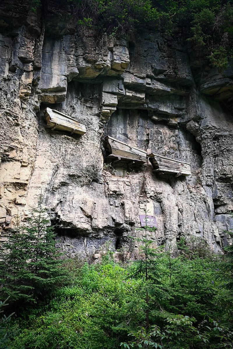 A photograph of three large wooden coffins attached to the side of a cliff.