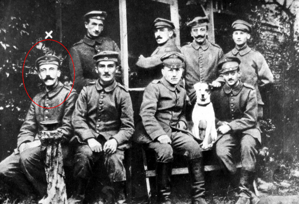 A group of eight soldiers in uniform and a dog on the Western Front during World War I. Adolf Hitler seen in the front row, at the far left.