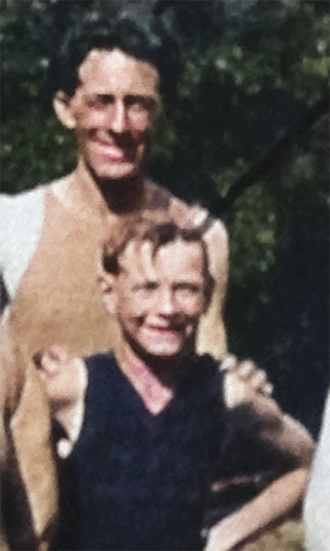 A colorized photograph of J.G. Tierney and his son Patrick Tierney standing in front of him. J.G. has his hands on Patrick's shoulders. They are both smiling. J.G. appears to be about 35 years old and Patrick is about 10.