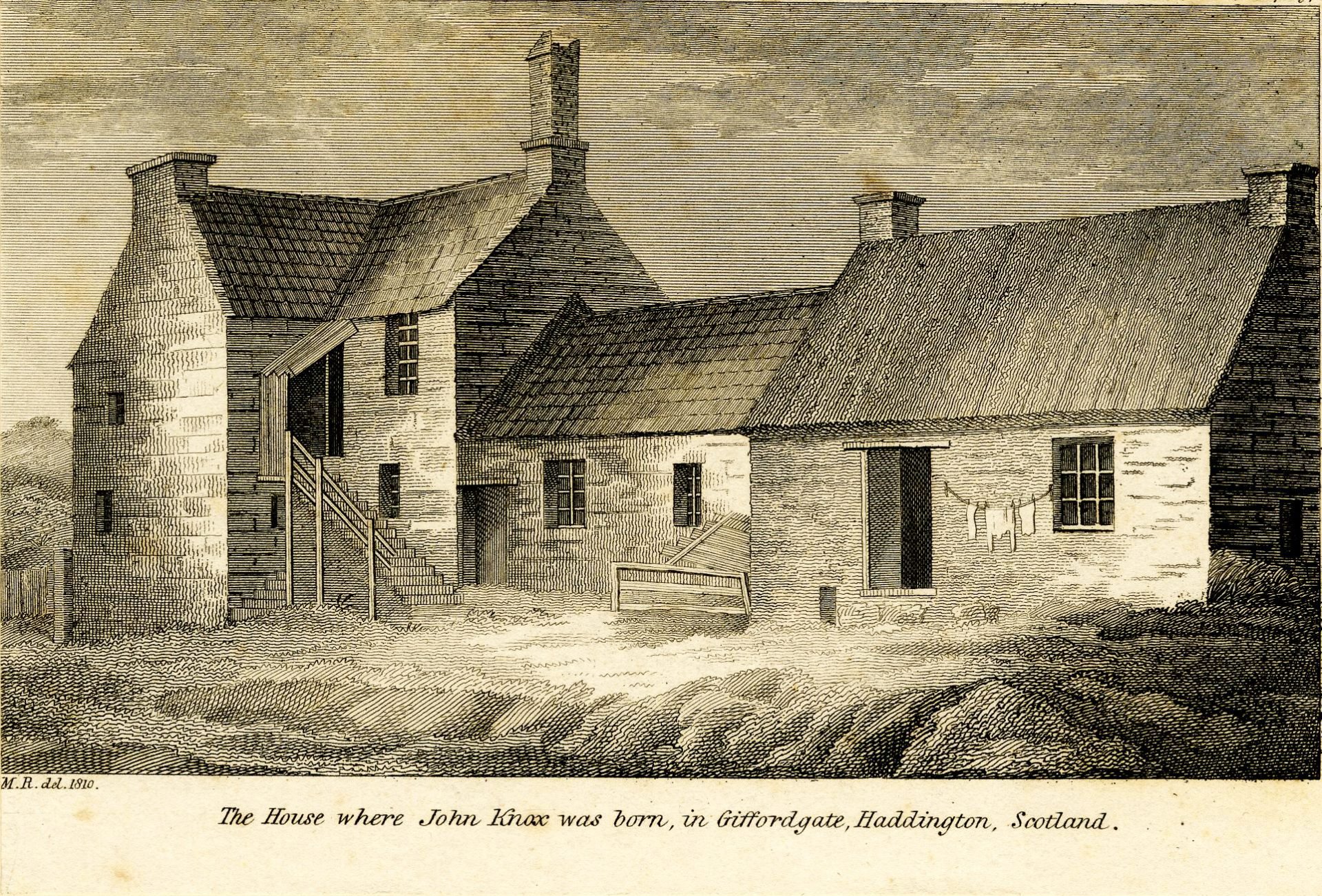 View of the house where Protestant Reformer John Knox was born, steps leading to the entrance on the left, and a line of clothes hanging on a wall between door and window to the right.