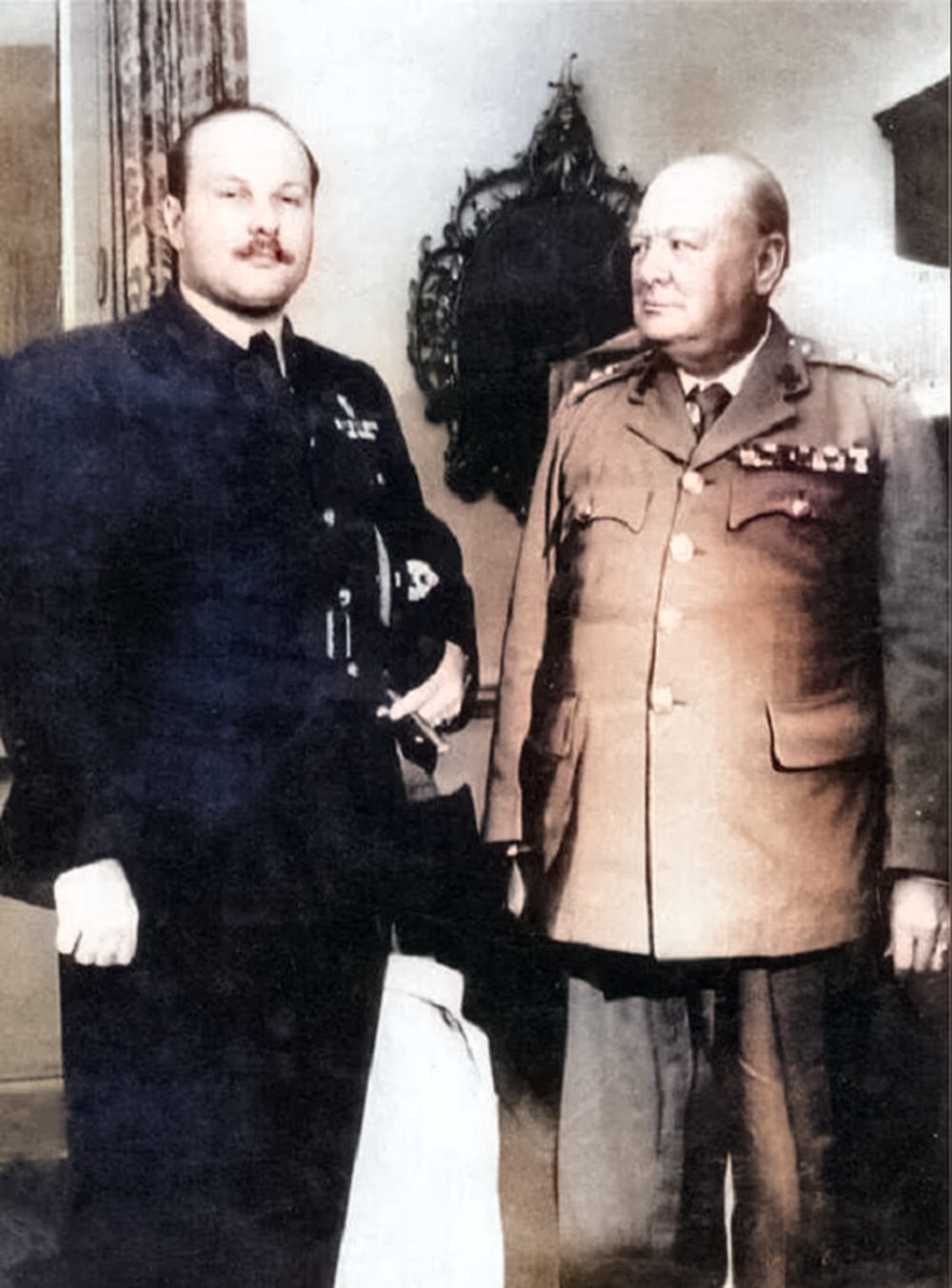A photograph of two men in military uniforms standing next to each other. The first man is dressed in a blue military uniform and the second man is dressed in a beige military uniform with medal ribbons on his chest.