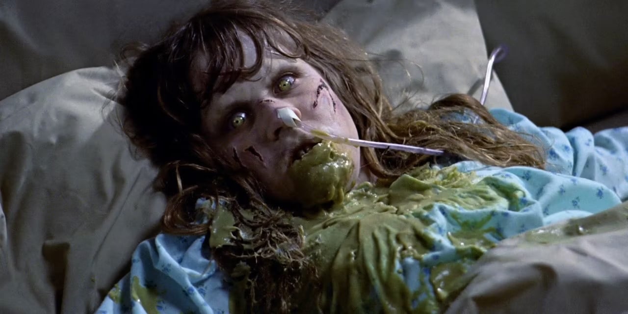 A still image from the film The Exorcist featuring a possessed girl with gray skin and bright green eyes, pee soup all over her.