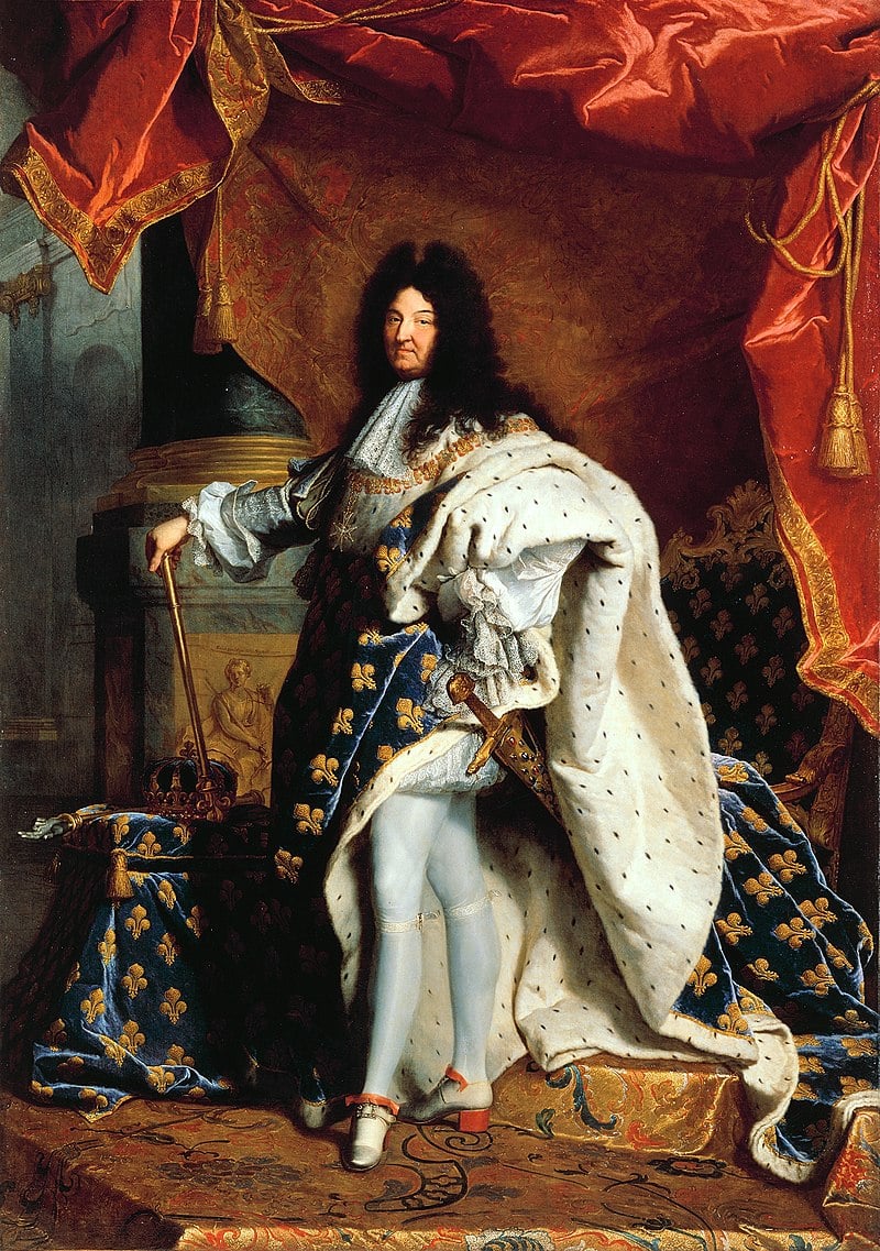 Portrait of Louis XIV in Coronation Robes embroidered with the royal fleur de lys along with some key elements of Baroque style such as the cravat, red heels, and the wig.