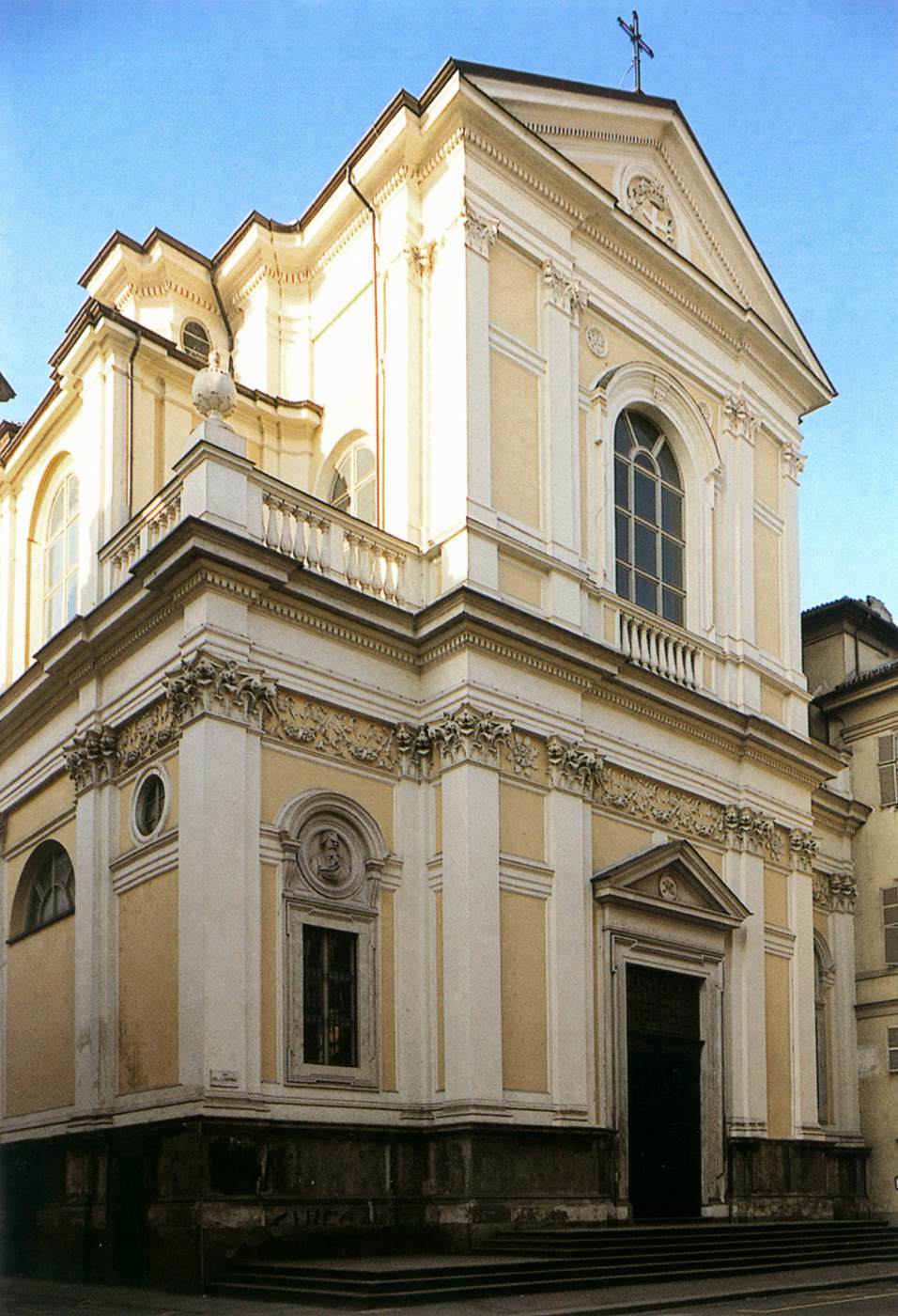 A photograph of The Church of Our Lady of Carmine in Turin, showcasing a beige facade with white columns and decorative details.