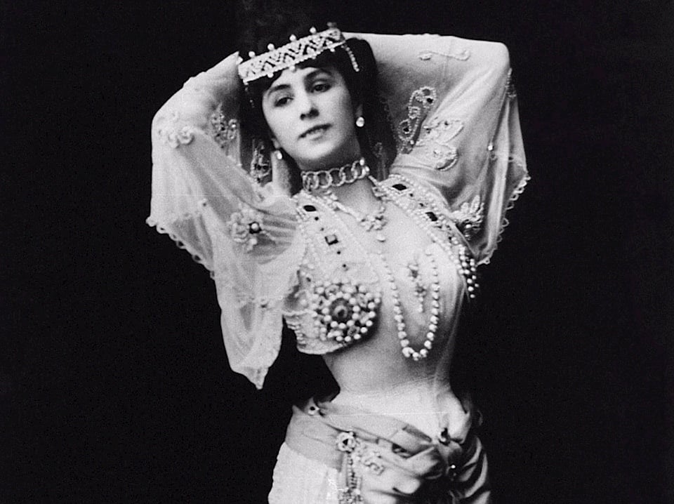 A photograph of a early 20th century dancer, dressed in an elaborate costume covered in pearls and jewels.