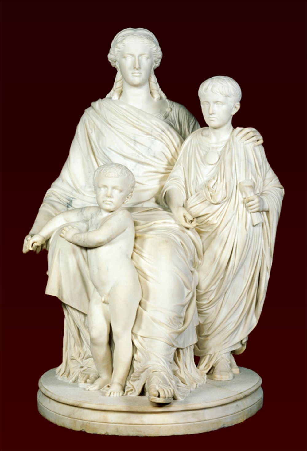 A white marble statue of three figures in robes on a round base The central figure is Cornelia Africanus, Mother of the Gracchi, figure on the left is a child Gaius Gracchus, Tiberius Gracchus is on the right is standing and holding a scroll, and the background is dark red.