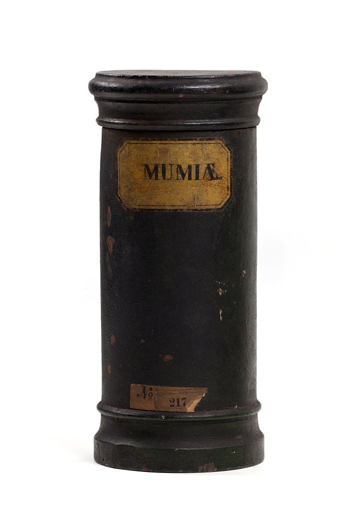 A photograph of an apothecary container labelled "Mumia". The container is made of wood and it is cylinder shaped.