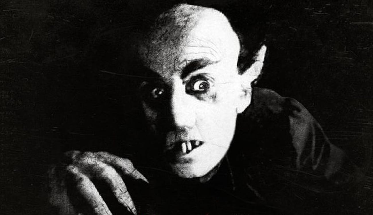 Still image from Nosferatu featuring a haunting vampire with long ears and fingers and sharp teeth.