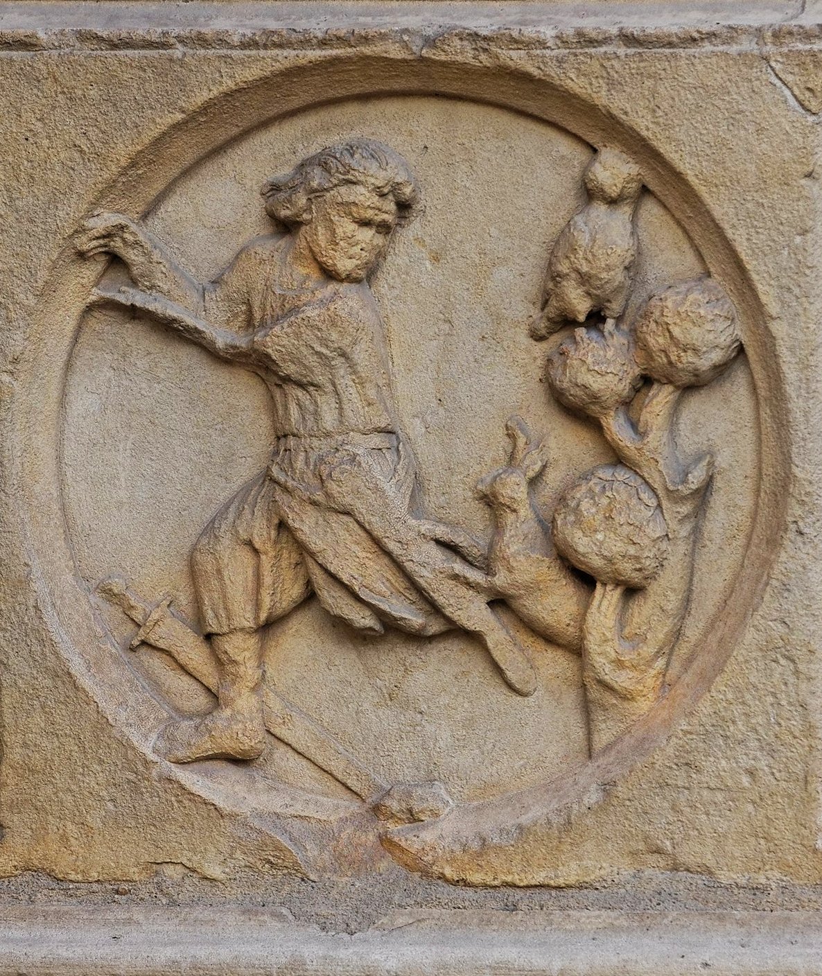 A stone relief sculpture of a knight on a Notre Dame de Paris façade running away from a rabbit. The sculpture is old and has some cracks and chips in it.