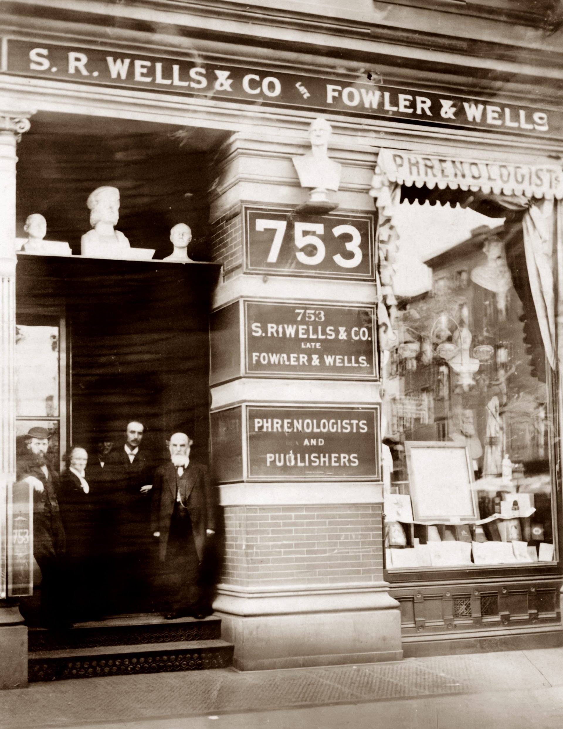 Samuel R. Wells, Charlotte Fowler Wells, Lorenzo N. Fowler, and two other men stand at the entrance of S.R. Wells & Co., previously known as Fowler & Wells, Phrenologists and Publishers.