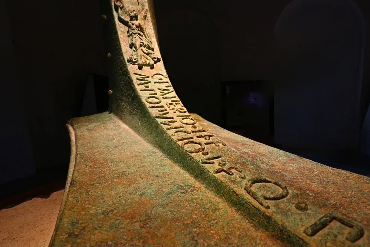 Photo of a Roman rostrum in bronze with an inscription in a dark room.