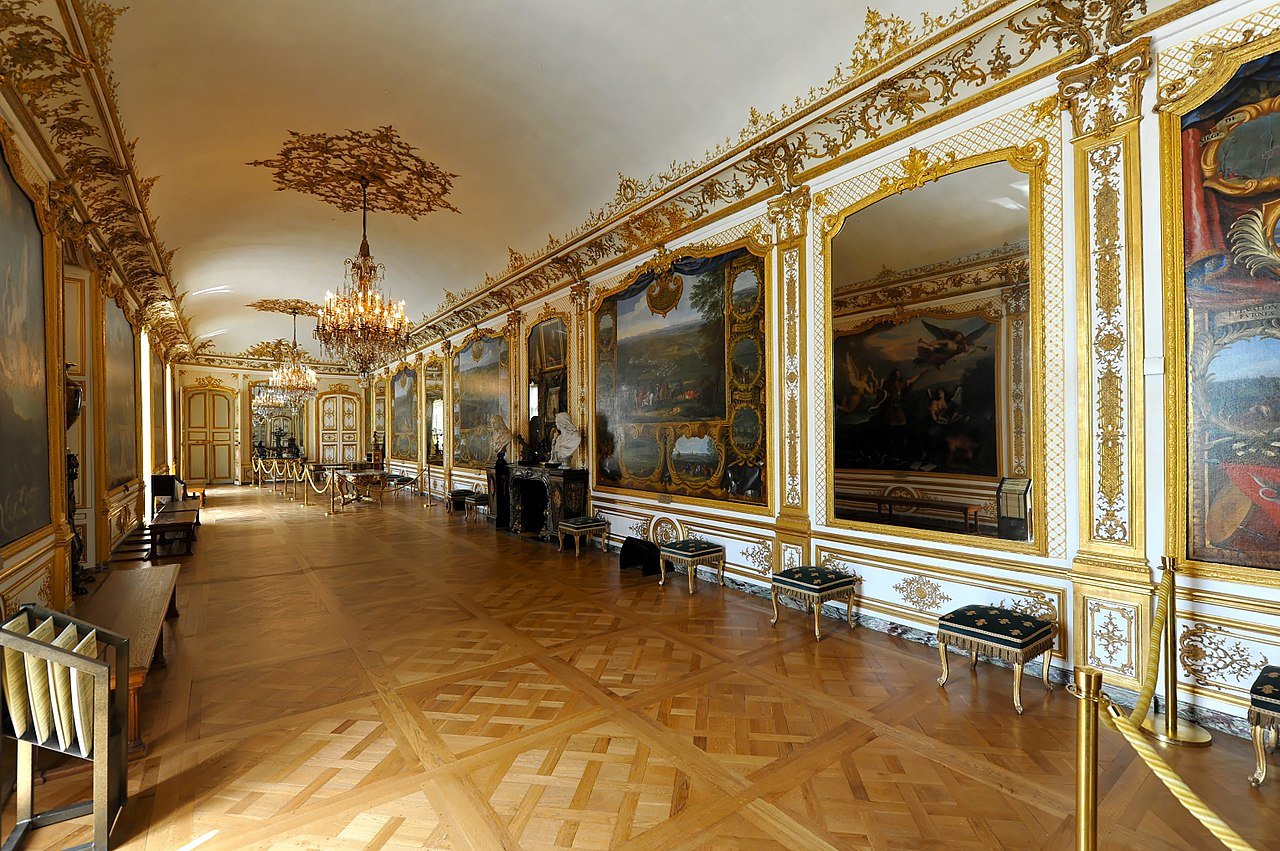 A photo of an opulent Rococo salon showcasing mirrors on one side and paintings on the other side.