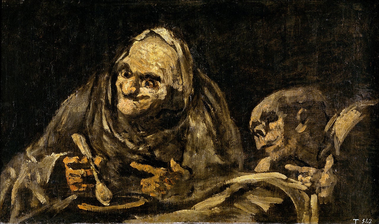 A painting of two grotesque figures, one looks like an old man the other like a skeleton. They are sitting at a table. The old man is eating from a bowl of soup. The background is dark and there are no other objects in the room.