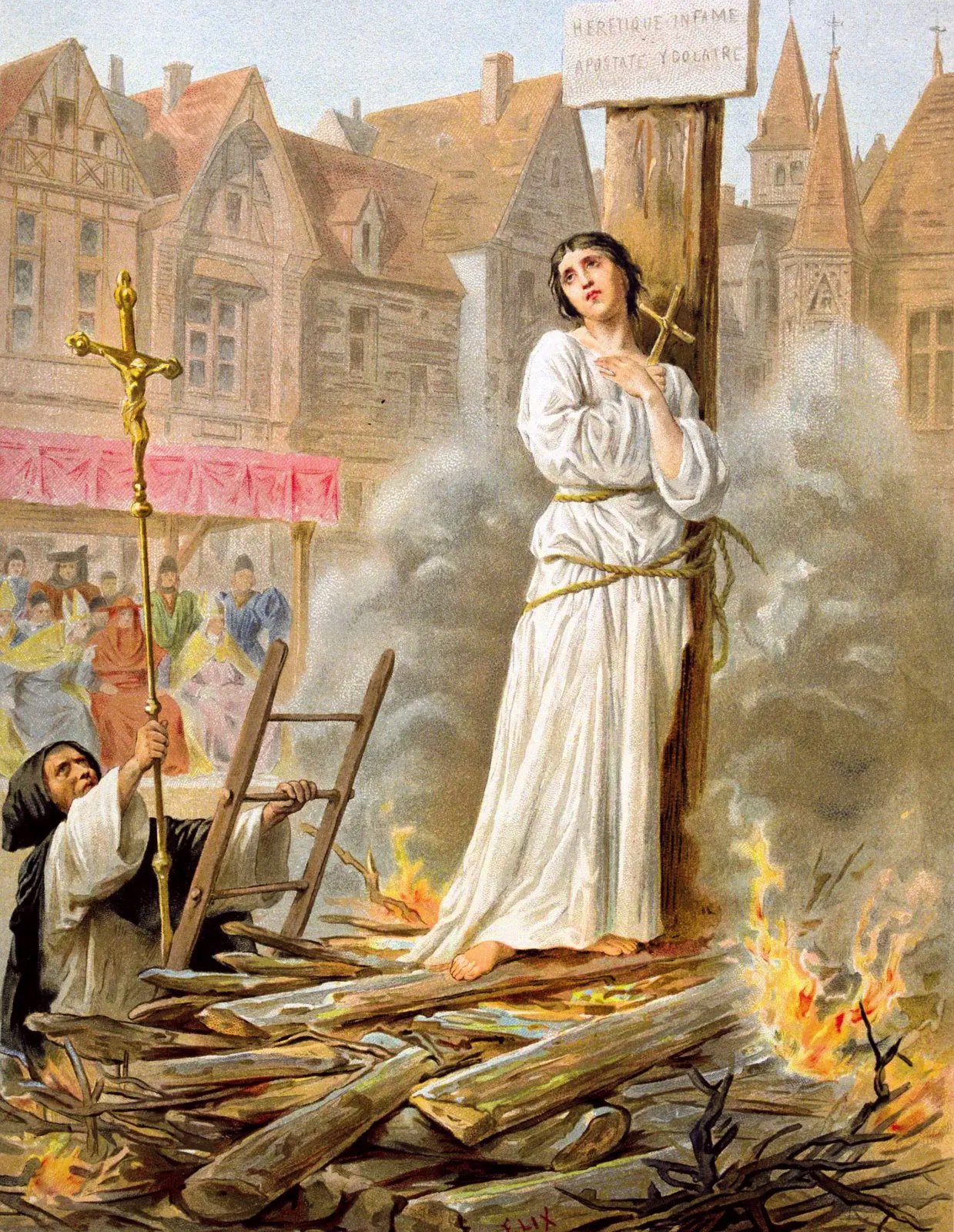 A medieval painting of Joan of Arc tied to a stake with a fire burning below her. She is wearing a white robe and is tied to the stake with rope. The background is a medieval town with buildings and people watching the scene. The text on the top right corner of the image reads “Heretique enflamme” (Heretic on fire).
