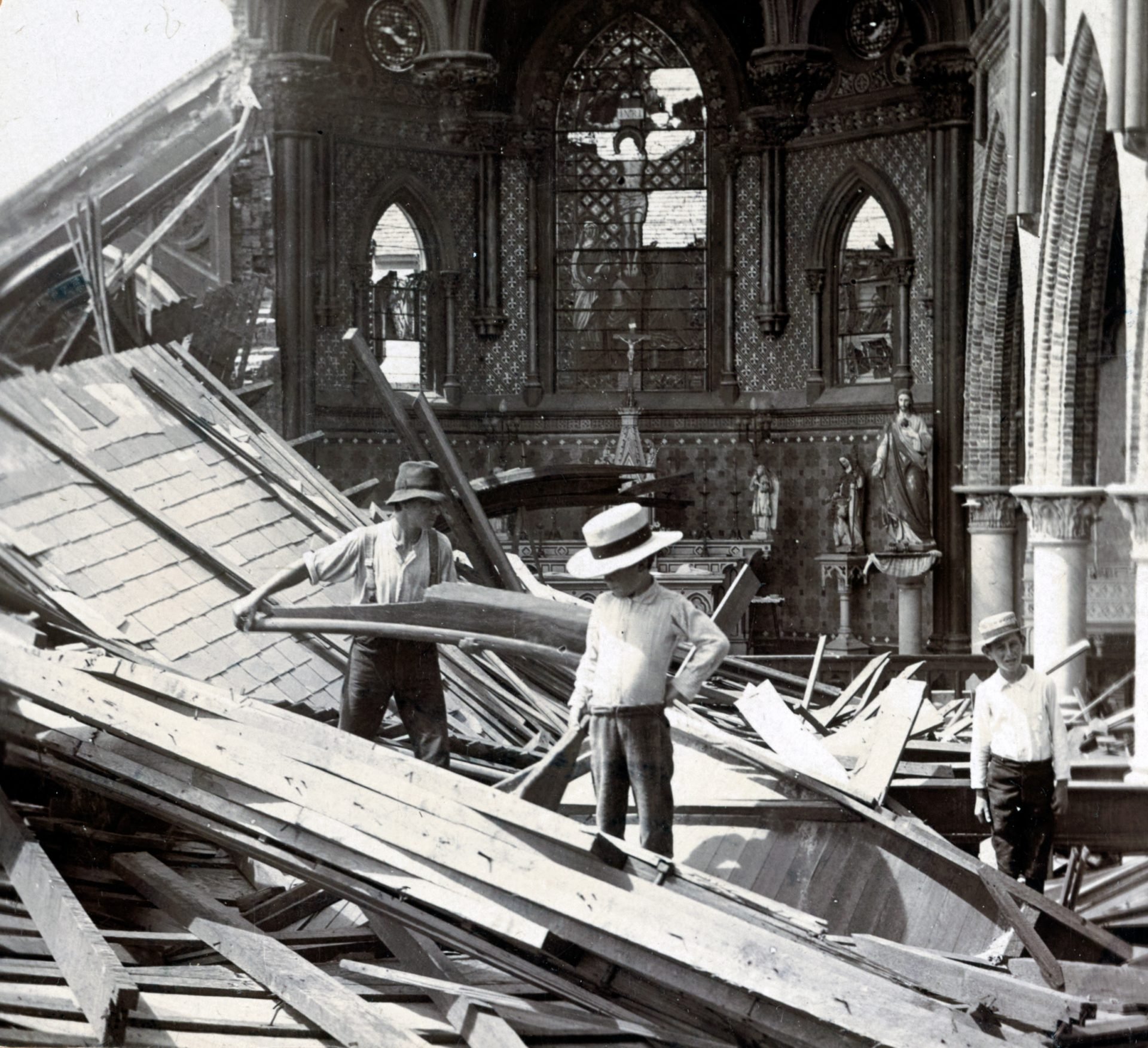 Three young men standing on a pile of debris inside a damaged church with an intact altar and stained glass window in the background.