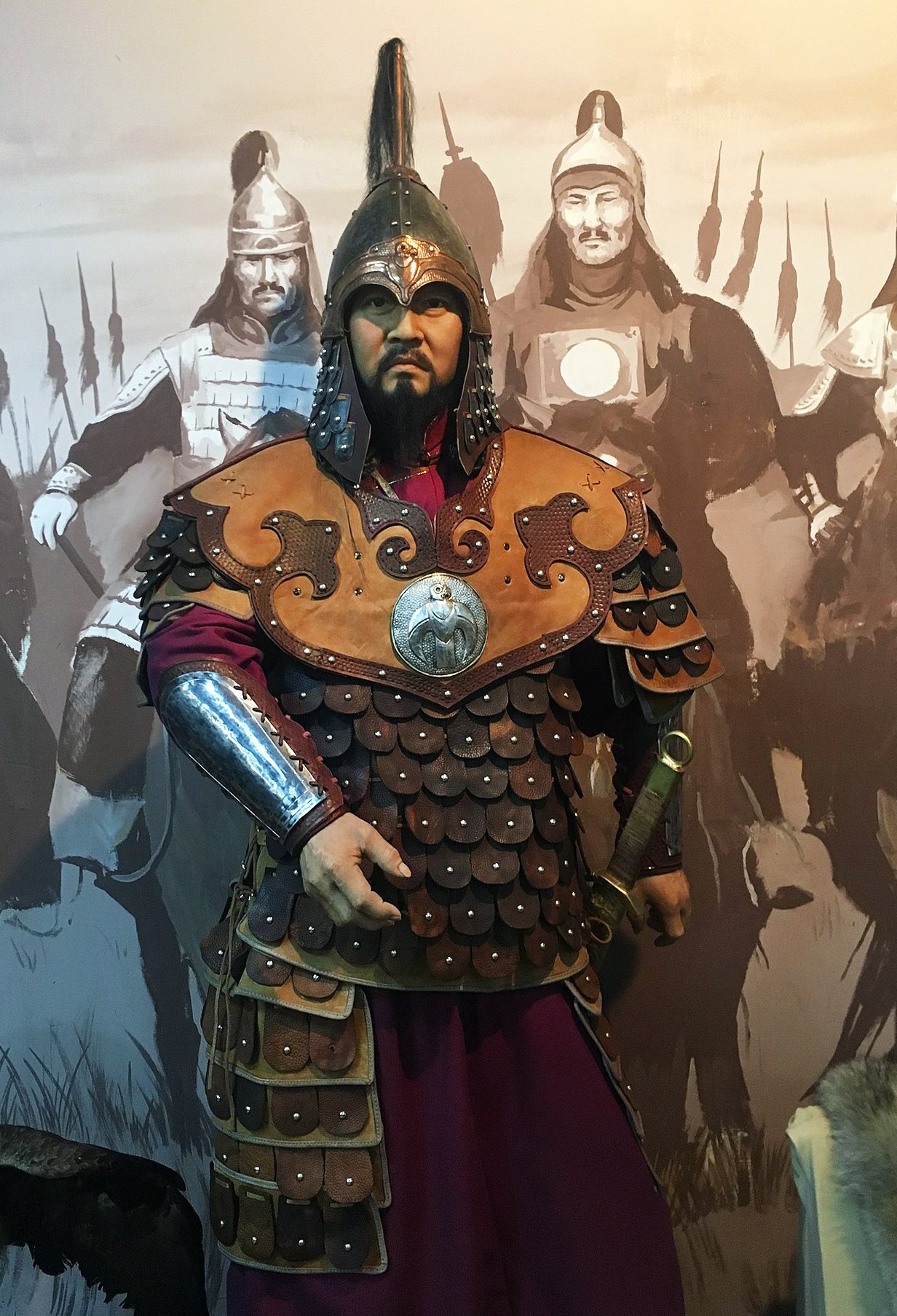 A photo of the figure of Subutai wearing mongolian armor in front of a mural of a battle scene. The armor is metal and leather, with a helmet that has a plume and a breastplate with an emblem.