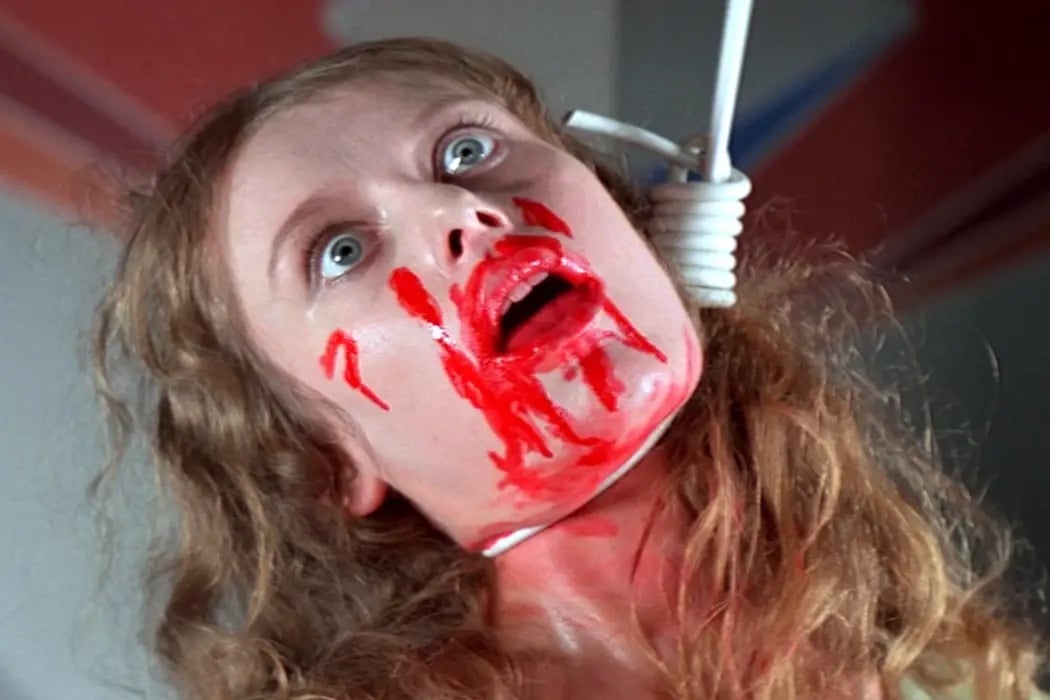 A still image from the film Suspiria featuring a close up shot of a woman's face, hanged by her neck with blood around her mouth.