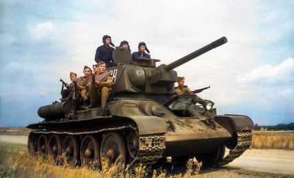 A historical photo of a group of Soviet World War II soldiers on a green T-34 tank with the number 28 in a field with trees and a blue sky.