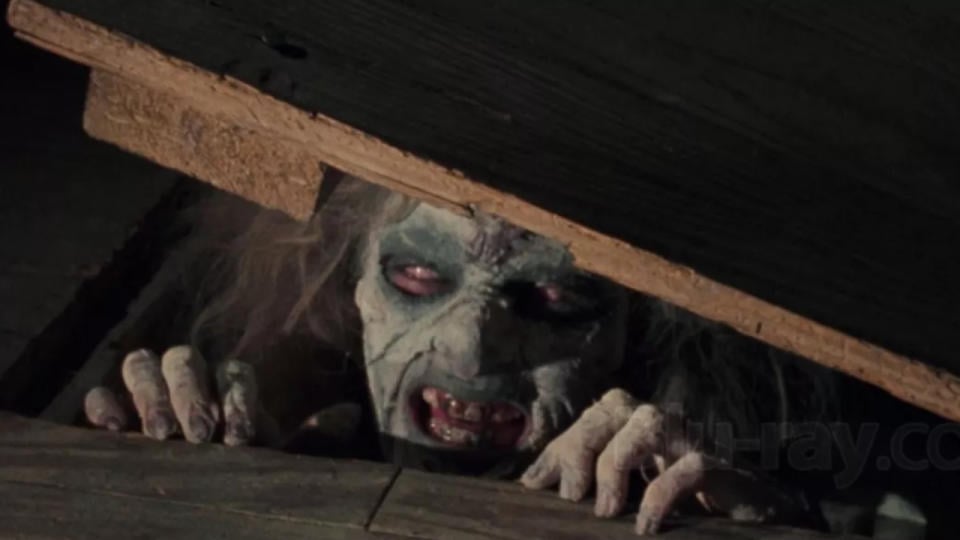 A possessed woman peaking from under a cellar door.