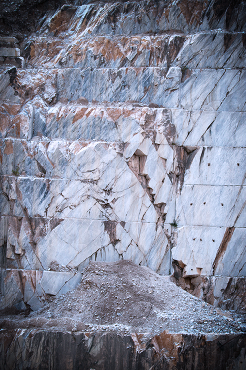 A photograph of one of the walls of a marble quarry, the light gray stone is cut in a systematic way.