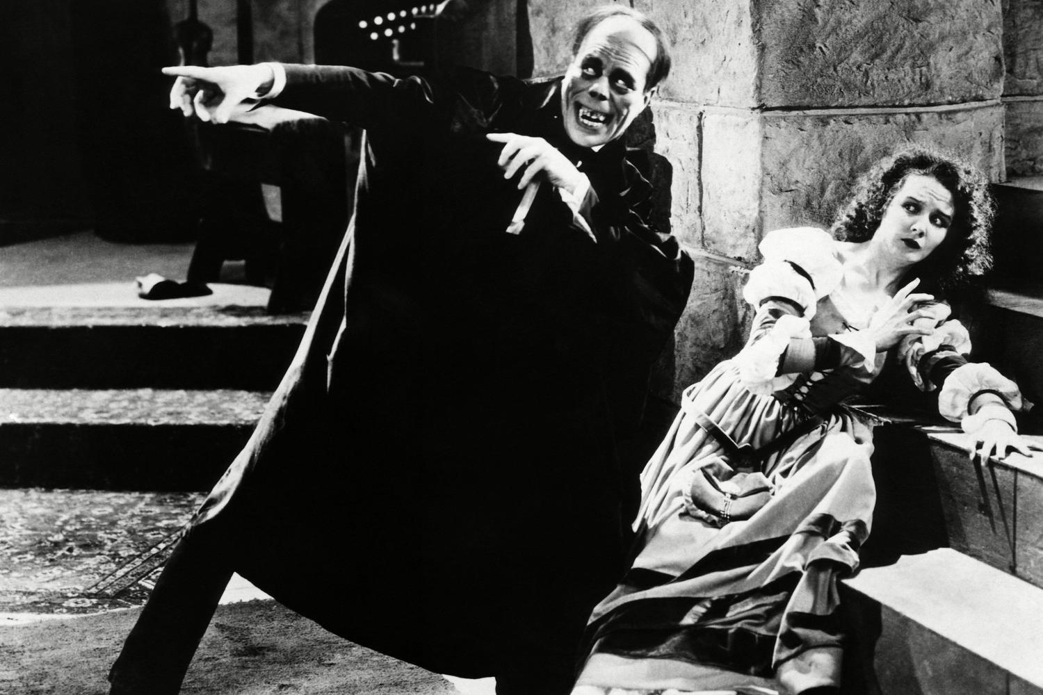 A still from the file Phantom of the Opera featuring a striking scene of the sinister looking man pointing off camera and a shocked woman sitting on steps.