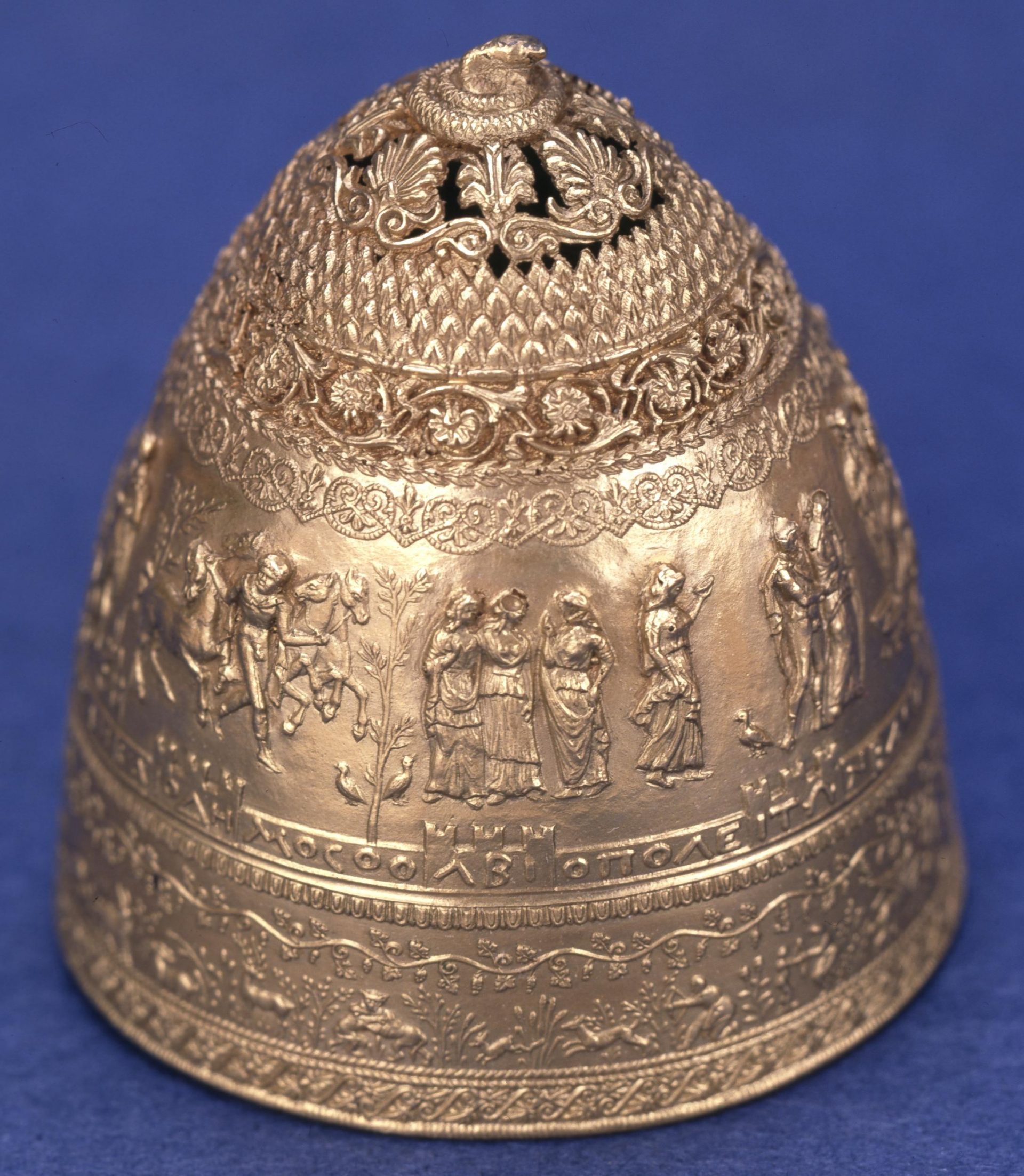 A photograph of an ancient gold crown. The crown appears to be Greek in origin and is cone shaped with figures and shapes decorating its surface.
